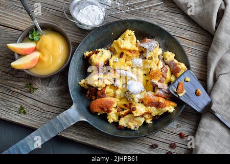 Kaiserschmarrn traditionnel viennois, crêpes sucrées déchiquetées avec raisins secs, servies dans une poêle à frire en fer sur de vieilles planches en bois sur une assiette en ardoise Banque D'Images