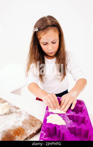 Petite fille formant des gâteaux doux, fond blanc Banque D'Images