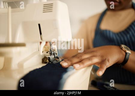 Gros plan des mains de tailleur à l'aide d'une machine à coudre. Couturier alimentant le denim à travers la machine à coudre. Main d'une couturière couture d'un morceau de Banque D'Images