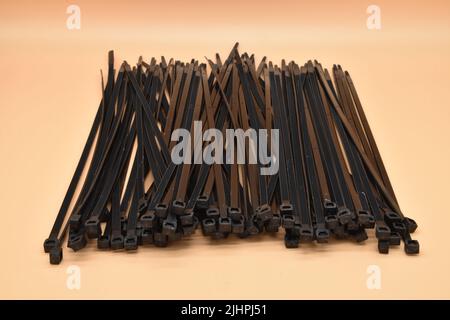 Serre-câbles noirs isolés sur fond orange. Attaches en plastique. Banque D'Images