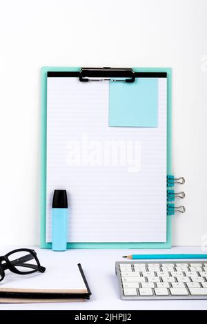 Message important présenté sur le presse-papiers du bureau avec bloc-notes, trombones, marqueur, lunettes et clavier. Informations de base écrites sur papier Banque D'Images