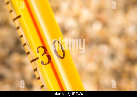 Thermomètre à alcool en verre en gros plan sur sable grossier, avec une lecture de 30+ C. pour la vague de chaleur estivale 2023, la vague de chaleur britannique, le temps chaud, les températures élevées, la chaleur intense Banque D'Images