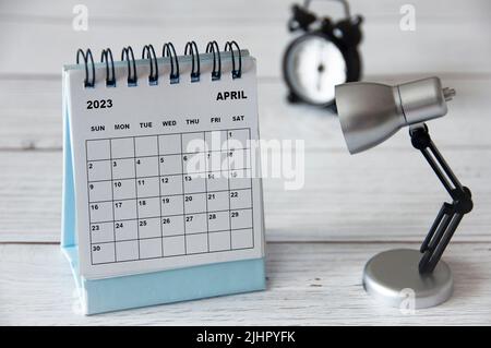 Calendrier du bureau blanc d'avril 2023 avec lampe de table sur table en bois. Concept de calendrier Banque D'Images