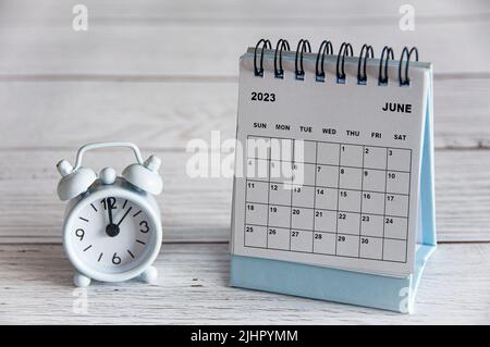 Le calendrier du bureau blanc du 2023 juin sur une table en bois avec un réveil pointant à 12 heures. Banque D'Images