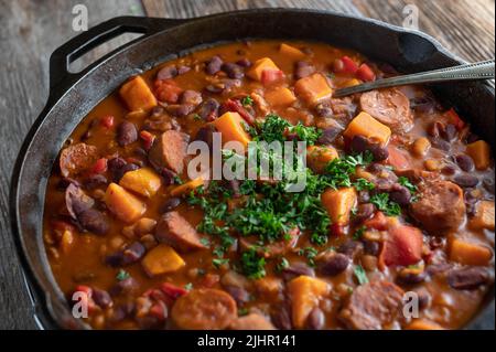 Ragoût de haricots mexicains avec chorizo salami, patates douces et légumes dans une casserole en fonte isolée sur une table en bois Banque D'Images