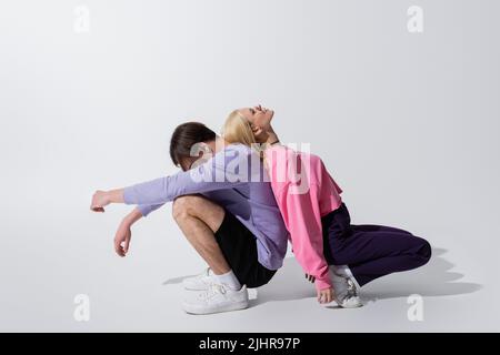 Vue latérale d'un couple en sweat-shirts se posant dos à dos sur fond gris Banque D'Images