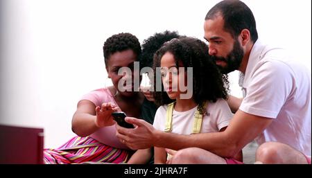 Famille multiethnique utilisant un téléphone cellulaire. Parents interraciaux et enfants de race mixte regardant l'écran de smartphone ensemble Banque D'Images