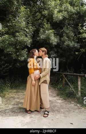 Vue latérale de l'homme embrassant femme enceinte sur le chemin dans la forêt Banque D'Images