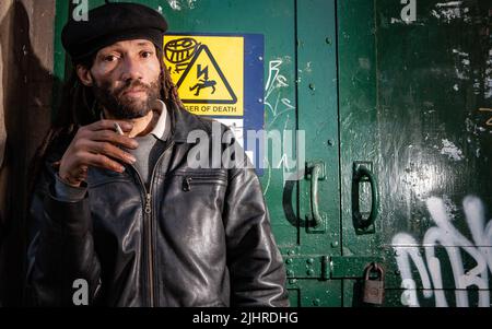 Street Life; Smoker. Un personnage sans-abri qui fume une cigarette dans une rue arrière de Londres. D'une série avec le même modèle. Banque D'Images
