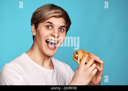 Jeune homme très affamé tenant un savoureux hamburger Banque D'Images