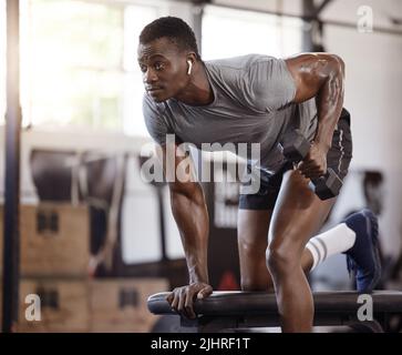 Un athlète américain sérieux de levage dumbbell en tricep curl entraînement sur le banc dans la salle de gym. Entraînement d'homme noir fort, ajusté et actif avec poids à l'intérieur Banque D'Images