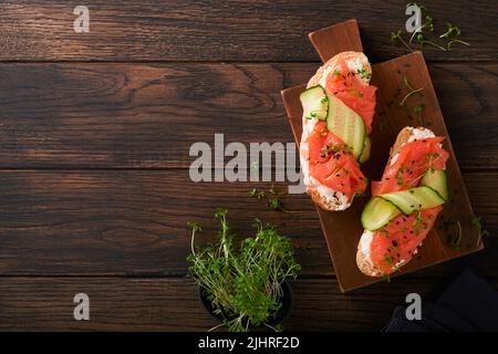 Sandwichs. Toast au saumon avec fromage à la crème, concombre, sésame noir et microverts sur fond de table en bois. Fruits de mer. Une alimentation saine. Photographie Banque D'Images