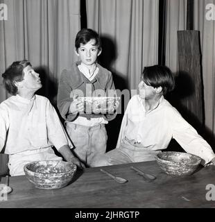 1970s, historique, trois enfants hommes acteurs avec des bols dans la scène musicale, Oliver, Angleterre, Royaume-Uni. Écrit par Lionel Bart, le spectacle de scène de l'âge est basé sur le roman de 1838 'Oliver Twist', du célèbre dramaturge anglais Charles Dickens. Le personnage du centel est Oliver, un garçon malnutris, un orphelin dans une maison de travail, qui, après avoir été apprenti à un sous-preneur, s'échappe à Londres où il se mêle à des voleurs à tout petits et des pickpockets. Banque D'Images