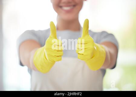 Un travailleur domestique méconnaissable montrant les pouces tout en portant des gants et en nettoyant. Une femme de race mixte inconnue qui a l'air heureuse pendant son nettoyage Banque D'Images