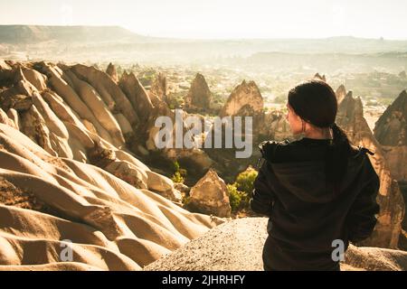 Un stand de femme attentif vous permet de regarder la vallée spectaculaire sur un lever de soleil brumeux avec des cheminées de fées en arrière-plan. Exploration solo en Turquie. Cinéma Banque D'Images