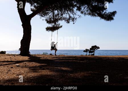 Garçon sur un arbre balançoire près de la mer lors d'une journée d'été sur Veli Rat, île de Dugi otok, Croatie Banque D'Images