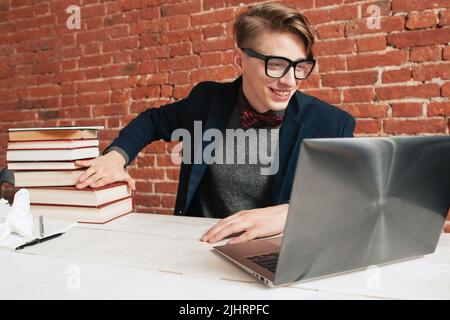 Homme souriant avec ordinateur portable, éloignez-vous d'une pile de livres Banque D'Images