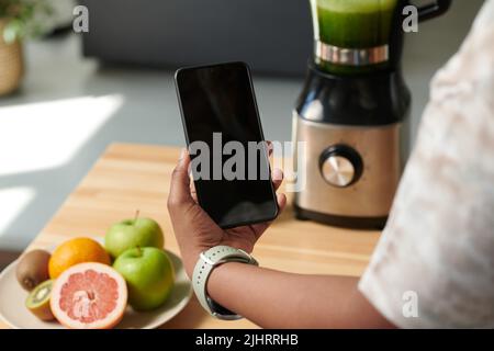 Gros plan d'une fille utilisant son smartphone pour allumer le blender en ligne et réaliser un smoothie frais Banque D'Images