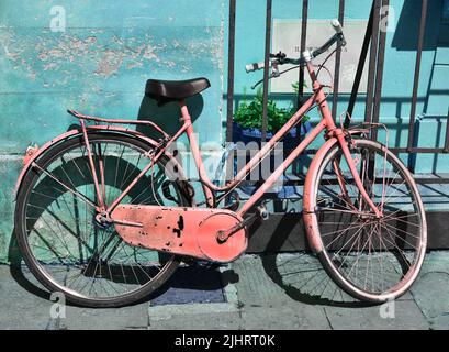 Un vélo rouge rouillé appuyé sur le mur bleu du bâtiment et la porte en métal Banque D'Images