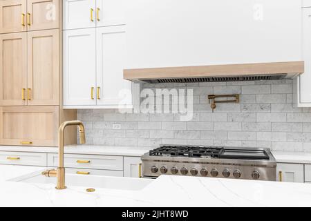 Un détail de cuisine avec un robinet d'or, des armoires blanches et en bois, un comptoir en marbre et un dosseret de carreaux de métro. Banque D'Images