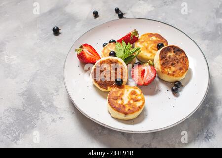 Crêpes au fromage cottage, beignets de ricotta ou syrniki avec cassis et fraises. Petit déjeuner sain et délicieux. Banque D'Images