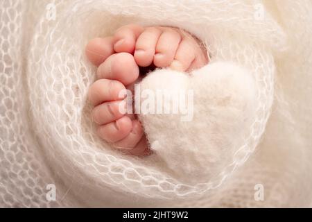 Coeur blanc tricoté dans les jambes d'un bébé. Gros plan des orteils, des talons et des pieds d'un nouveau-né. Banque D'Images