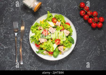 Salade de thon avec laitue, tomates cerises, concombre et maïs sur fond de pierre noire. Vue de dessus Banque D'Images