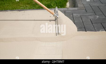 Pose de la pierre de pavage. Le maître pose les pavés en couches. Pose de dalles de béton dans la cour de la maison sur un sable Banque D'Images