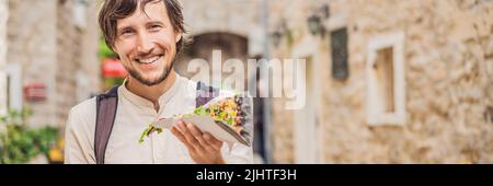 BANNER, LONG FORMAT Jeune homme touristique manger une pizza traditionnelle dans la vieille ville de Budva. Concept de voyage au Monténégro Banque D'Images