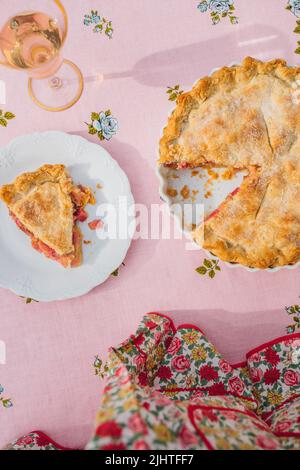 une seule tranche de tarte à la rhubarbe sur plaque blanche, nappe rose avec roses bleues Banque D'Images