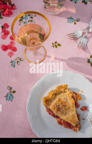 une seule tranche de tarte à la rhubarbe sur plaque blanche, nappe rose avec roses bleues Banque D'Images