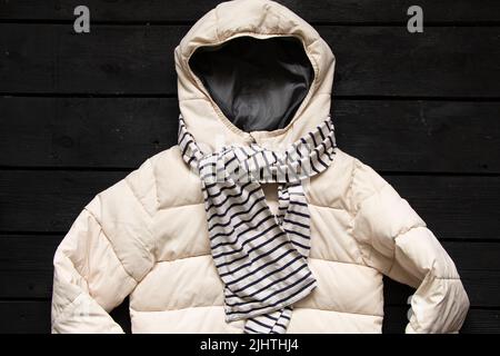 blouson chaud blanc hiver pour femme et foulard rayé noir et blanc se trouvent sur une table en bois noir, des vêtements d'hiver, une veste Banque D'Images