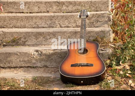 la vieille guitare brune se trouve dans le parc sur les marches de l'automne au soleil, guitare Banque D'Images