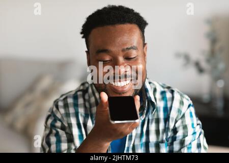 Homme africain joyeux utilisant la recherche vocale sur smartphone à la maison Banque D'Images