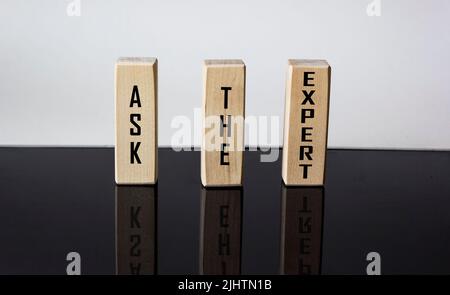 DEMANDEZ À L'EXPERT écrit sur des blocs de bois et un fond noir et blanc avec réflexion Banque D'Images