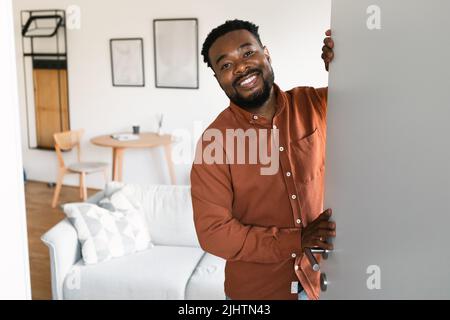 Homme africain ouvrant la porte souriant à la caméra debout à la maison Banque D'Images