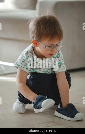 Enfant avec l'autisme dans les lunettes de jeu avec ses chaussures Banque D'Images