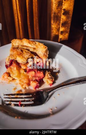 demi-tranche de tarte à la crème de rhubarbe mangée sur plaque blanche avec fourchette et fond de rideau doré Banque D'Images