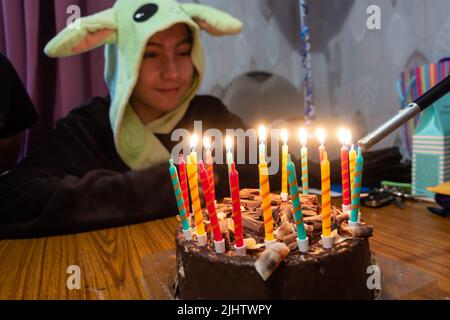 Bougies sur un gâteau d'anniversaire au chocolat allumé à l'aide d'un briquet à gaz que le garçon d'anniversaire regarde. Banque D'Images