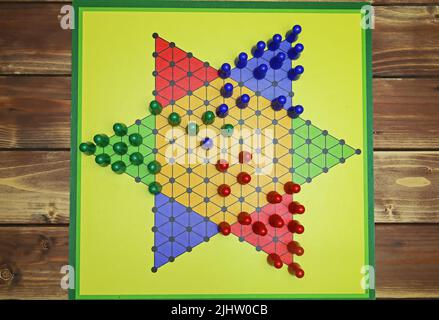 Vue de haut en bas sur un tableau de jeu jaune isolé avec des pièces de jeu hexagonales, multicolores, fond en bois - pions chinois (sternhalma) Banque D'Images