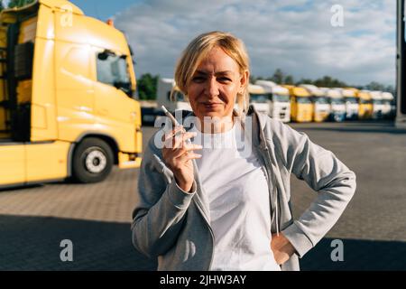 Femme originaire du Caucase d'âge moyen travaillant comme conducteur de camion. Fumer sur un parking de camions Banque D'Images