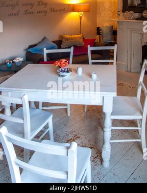 Chambre avec table en bois blanc et chaises sur parquet usé avec lampe et cheminée et canapé avec coussins Banque D'Images
