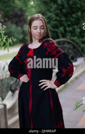 charmante jeune femme ukrainienne en robe nationale rouge et noire brodée à l'extérieur. jolie fille dans le parc portant vyshyvanka. Banque D'Images