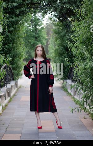 charmante jeune femme ukrainienne en robe nationale rouge et noire brodée à l'extérieur. jolie fille dans le parc portant vyshyvanka. Banque D'Images