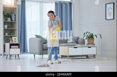 La musique fait tout ce qu'il y a de mieux. Une jeune femme écoute de la musique tout en passant le sol à la maison. Banque D'Images