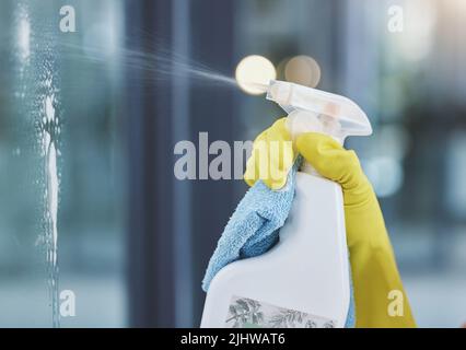 Vaporisez et polissez. Une femme méconnaissable nettoie la fenêtre de son appartement. Banque D'Images