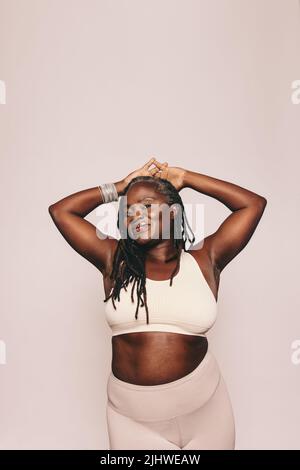 Femme sportive regardant la caméra tout en se tenant debout sur un fond gris. Femme mature avec des dreadlocks portant des vêtements de sport dans un studio. Milieu- Banque D'Images