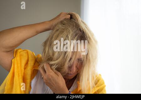 Femme blonde dans ses 50s cheveux rouffling. Concept de maladie mentale ou de déséquilibre émotionnel. Banque D'Images