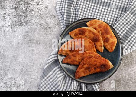 Chebureau - tartes frites ou dindes poêlées avec de la viande et de l'oignon sur une assiette ronde sur fond sombre. Vue de dessus, plan d'appartement Banque D'Images