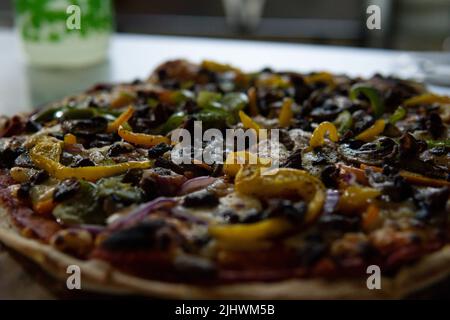 Gros plan d'une pizza fraîchement cuite avec de la viande, des oignons, des champignons et des poivrons verts et jaunes sur une table en bois. Pizza faite dans un four à bois. Pizza Banque D'Images